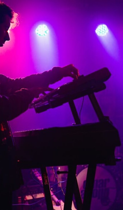 Cody Rowlett performing live on keyboards under magenta and blue stage lights